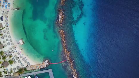 Tilt-up-aerial-view-of-Mambo-Beach-with-rock-breakwater,-Curacao,-Dutch-Caribbean-island