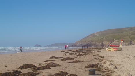 Turistas-En-La-Orilla-Arenosa-Con-Algas-Dispersas-En-La-Playa-De-Perranporth-En-Cornualles,-Inglaterra---Tiro-Ancho