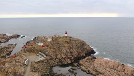 Lindesnes-lighthouse-ont-op-of-coastal-rock-with-north-sea-background-Norway---Slow-rotating-aerial-approaching-and-descending-while-keeping-lighthouse-in-center-of-frame---people-walking-around