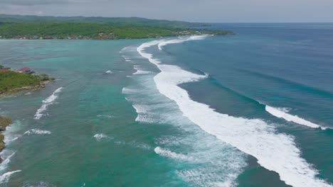 Long-rolling-waves-towards-shore-of-Nusa-Lembongan-and-Ceningan,-aerial
