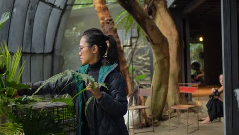 Asian-woman-smiles-while-organizing-leaf-and-plants-on-dining-table