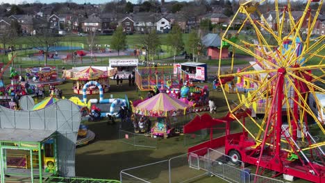 Small-town-fairground-Easter-holidays-funfair-rides-in-public-park-Ferris-wheel-pan-left-aerial-view