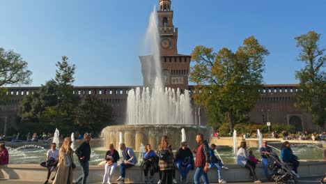 Tilt-up-of-medieval-Sforza-Castle-in-Milan-with-tourists-at-fountain-edge-and-bicycle-passing