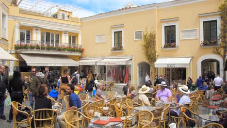 Panning-across-medieval-European-style-architecture-in-historic-city-center-with-Umberto-Square-and-tourists-having-coffee-in-Capri,-Italy