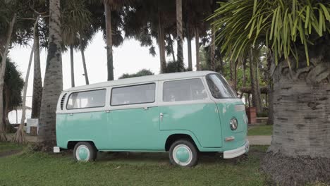 A-static-shot-of-a-classic-VW-van-parked-between-2-coconut-trees-on-a-beach-in-Pattaya,-Chon-Buri,-Thailand