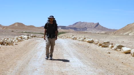 In-the-heat-of-the-day-a-man-walks-down-a-dusty-dirt-road-in-a-barren-landscape