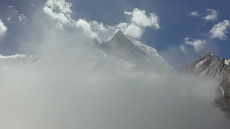 Epic-aerial-drone-shot-of-a-snowy-peak-of-the-Annapurna-mountains,-starting-in-clouds-then-revealing-the-mountains-in-Nepal