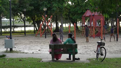 Dos-Damas-Indias-Hablan-En-El-Parque-Con-Vistas-Al-Parque-Infantil,-Parque-De-La-Playa-De-Changi,-Singapur