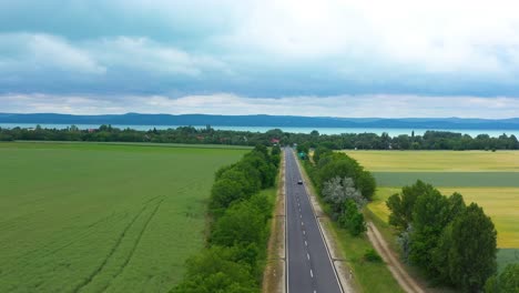 Auto-Fährt-Auf-Der-Autobahn-Zum-See-Mit-Wunderschönem-Regnerischen-Hintergrund,-Drohnenaufnahmen