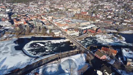 Kongsberg-city-bridge-connecting-city-above-Numedalslagen-river-in-Norway---Beautiful-sunny-morning-aerial-with-river-flowing-and-traffic-passing-on-roads