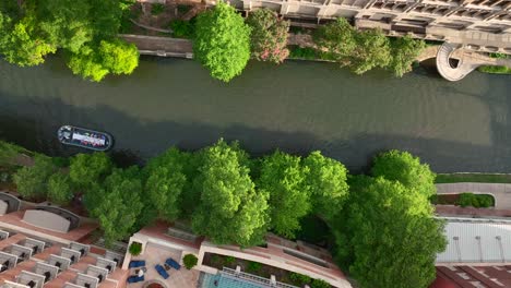 Drone-aerial-descending-on-San-Antonio-downtown-urban-River-Walk-park-with-barge-full-of-tourists