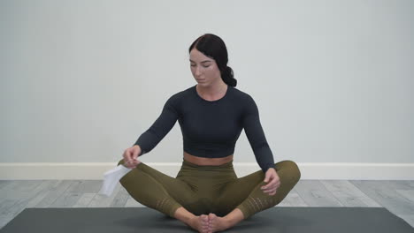 Young-woman-doing-yoga,-meditating-in-lotus-pose,-puts-on-medical-face-mask.-Female-athlete-doing-exercises-indoors.-White-background-and-copy-space.