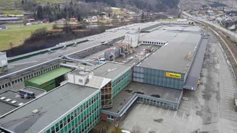 Nordan-door-and-window-factory-in-town-of-Moi-at-Lund-municipality-Norway---Aerial-flying-above-rooftop-of-industrial-building