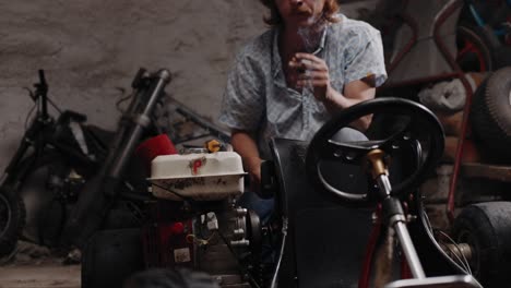 Filmaufnahme-Eines-Mechanikers,-Der-Einen-Go-Kart-Sitz-Inspiziert,-Während-Er-Eine-Zigarette-Raucht