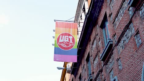 Bandera-Del-Arco-Iris-Lgtbq-Con-El-Logotipo-De-Ugt-Union-Colgando-De-Un-Edificio-De-Ladrillo-Al-Aire-Libre-En-Madrid,-España