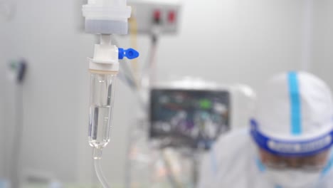 IV-Drip-In-Tube-With-Doctor-Wear-Infection-Control-Gown-In-Background,-Close-Up