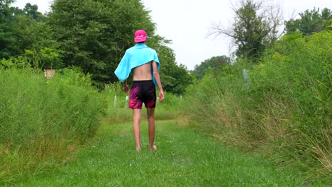 Tilt-up-shot-of-tall-man-walking-on-path-surrounded-by-shrubs-after-swimming-in-lake
