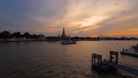 Touristenkreuzfahrtschiffe-Fahren-Bei-Sonnenuntergang-Entlang-Des-Flusses-Chao-Phraya-Mit-Dem-Tempel-Wat-Arun-Im-Hintergrund,-Bangkok-–-Malerischer-Zeitraffer