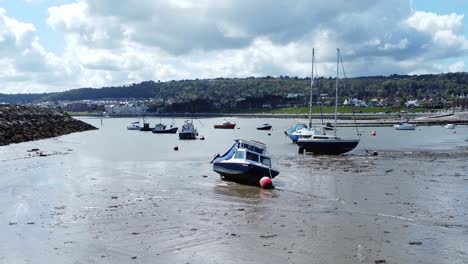 Aerial-view-moored-boats-on-Welsh-low-tide-seaside-breakwater-harbour-coastline-slow-right-descend-low