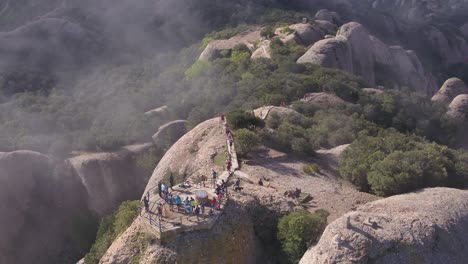 Aerial-rising-view-looking-down-at-running-event-top-of-Montserrat-rocky-tourism-mountain-summit-Spain