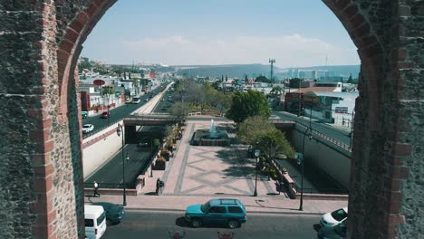 Aerial-view-of-drone-passing-through-queretaro-arches-at-midday