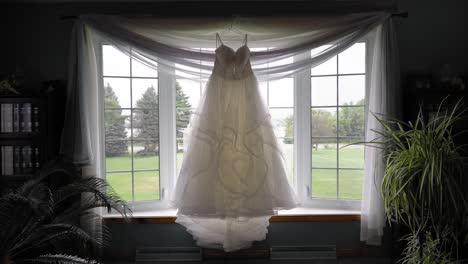 Gorgeous-white-designer-wedding-gown-hanging-in-a-well-lit-window-of-a-bedroom
