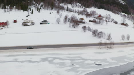 Cars-Driving-Through-Road-At-The-Edge-Of-Hillside-And-Frozen-Lake---aerial-shot