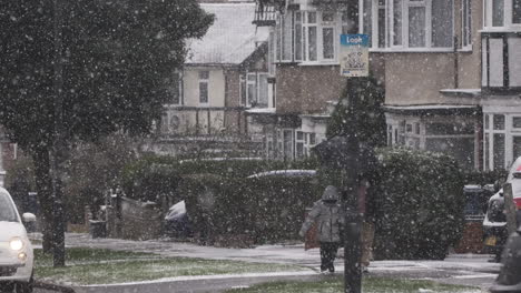 Mother-And-Child-Holding-Umbrella-On-Pavement-Whilst-Its-Snowing-With-Traffic-Going-Past