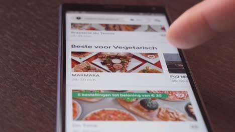 Zeigefinger-Einer-Person,-Die-Mit-Dem-Mobiltelefon-Auf-Einem-Holztisch-Durch-Die-Uber-Eats-App-Scrollt
