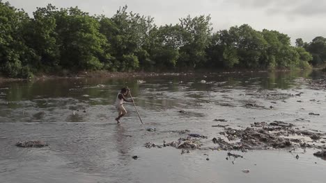 Boy-Walking-Through-A-River-Full-Of-Dumped-Garbage,-Environmental-And-Health-Issue
