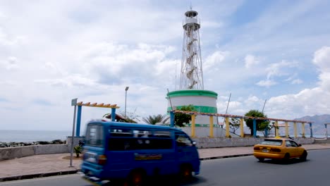 Green-and-white-Farol-lighthouse-landmark-and-traffic,-cars-and-scooters,-in-capital-city-Dili,-Timor-Leste,-Southeast-Asia