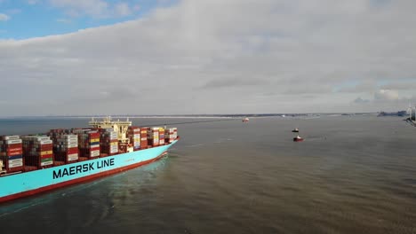 Ein-Riesiges,-Mit-Containern-Beladenes-Containerschiff-Fährt-An-Deck-In-Den-Hafen-Von-Rotterdam-Ein-Und-Zwei-Kleine-Schlepper-Warten-Darauf,-Das-Schiff-An-Einem-Teilweise-Bewölkten,-Ruhigen-Tag-Zu-Seinem-Liegeplatz-Zu-Bringen