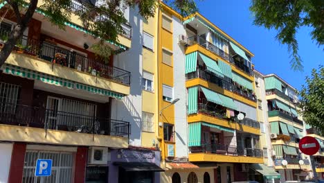 Typical-Spanish-street-with-apartments-and-houses-in-Marbella-old-town,-city-life-on-a-sunny-day-and-blue-sky-in-Spain,-4K-tilting-up