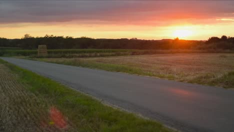 Small-rural-asphalt-road-with-agriculture-field-and-majestic-colorful-sunset-in-day-to-night-timelapse-shot