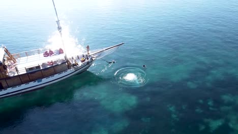 Men-diving-of-tourist-tour-ship-at-Pulau-Katangan-sandbank-coral-reef,-Aerial-hovering-shot