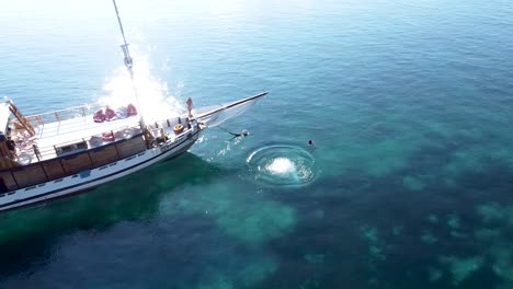 Hombres-Buceando-En-Un-Barco-Turístico-En-El-Arrecife-De-Coral-Del-Banco-De-Arena-De-Pulau-Katangan,-Tiro-Aéreo