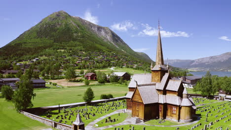 Iglesia-De-Madera-De-Lom-Con-Cementerio-En-Un-Día-Soleado-Con-Vistas-A-La-Montaña-En-Lom,-Condado-De-Innlandet,-Noruega