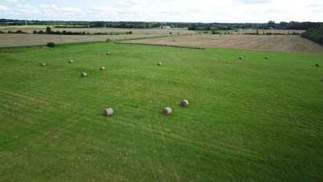Aerial-view-hay-bales-in-the-green-agriculture-field,-bailed-hay-drying-on-ranch-land,-the-straw-is-compressed-into-roles,-sunny-summer-day,-wide-drone-shot-moving-backward-high