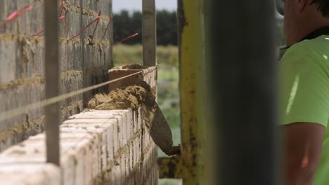 Bricklayer-Laying-Wet-Mortar-Cement-On-Housing-Brick-Wall-Construction,-SLOW-MOTION