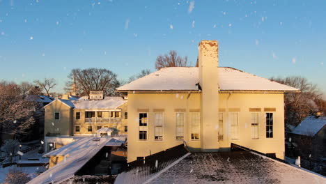 AERIAL-Fly-Over-Historic-Yellow-Brick-Building-During-Winter-Snowfall