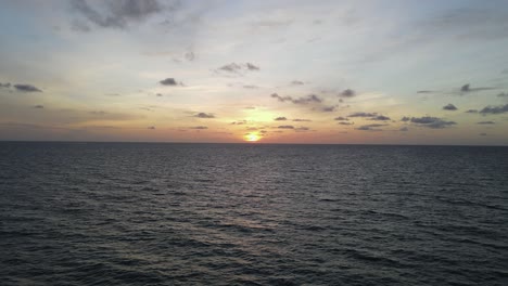 Rising-water-aerial-of-golden-sunrise-over-dark-blue-ocean-to-horizon