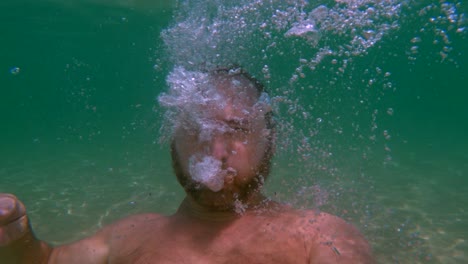 Underwater-view-of-bearded-man-breathing-out-air-to-create-bubbles