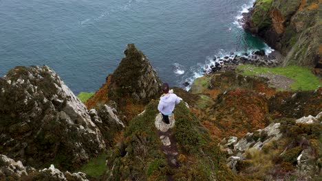 Male-Hiker-on-Dangerously-High-Edge-of-Cliff-of-Horn-Head,-Ireland---Aerial