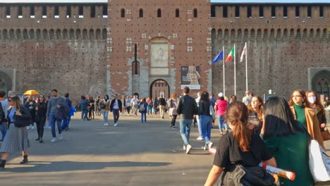 People-walk-toward-arched-gate-entrance-of-Sforza-Castle-in-Milan,-Italy