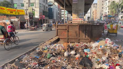 Road-side-garbage-dump-in-a-city-with-vehicles-and-a-street-dog,-pan-right-shot