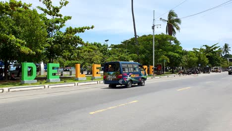 Ein-Farbenfroher-Blauer-Microlet-ÖPNV-Bus-Auf-Einer-Belebten-Straße-Mit-Beliebtem-Wahrzeichen-In-Der-Hauptstadt-Dili,-Timor-Leste,-Südostasien
