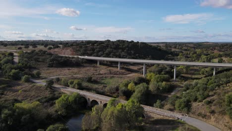 Aerial-forward-over-old-roman-bridge-and-modern-elevated-road-in-background,-Vila-Formosa-in-Portugal