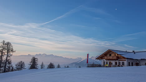 Time-lapse-shot-of-beautiful-sunrise-on-top-of-snowy-mountains-in-the-morning---Wooden-Cottage-with-waving-austrian-flag---Alps,Austria