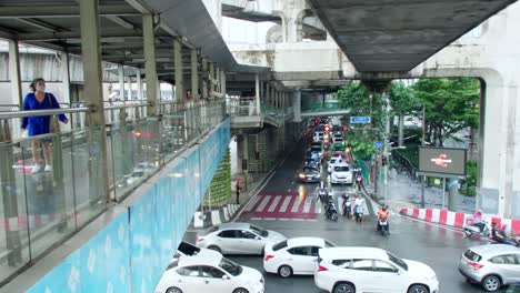Gente-Caminando-En-La-Pasarela-Sobre-El-Tráfico-A-Través-De-Intersecciones-Concurridas-En-Hora-Punta-En-Bangkok