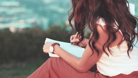 Faceless-woman-writing-in-her-journal-at-an-outdoor-location,-unrecognizable-brunette-female-with-book